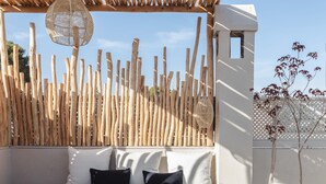Una mesa de madera con una cesta tejida y portavelas, un banco acolchado blanco con cojines negros, y una valla de madera con una cesta colgando de la parte superior.