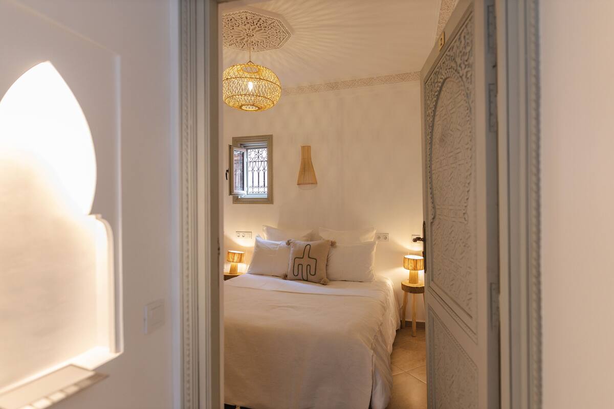 A bedroom with a bed, two bedside lamps, a window, and a decorative ceiling light.