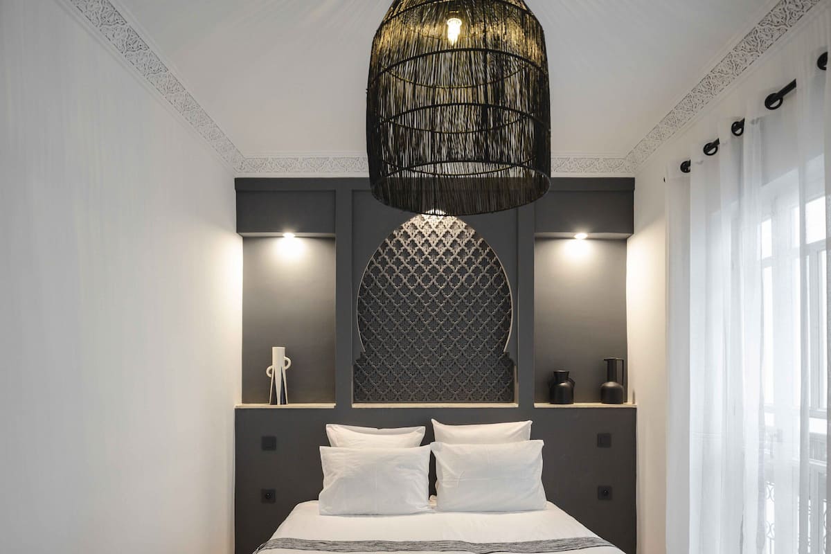 A bedroom with a bed, a chair, a decorative ceiling light, and a window with curtains.