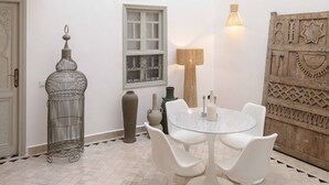 Un comedor con una mesa redonda y sillas blancas, una lámpara metálica decorativa y una pared con estampado.
