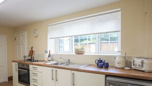 A kitchen with white cabinets, a stainless steel dishwasher, a double sink, and a window with a view of the outside.