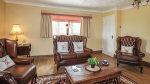 A living room with two leather armchairs, a wooden coffee table, and a red and white checkered window valance.