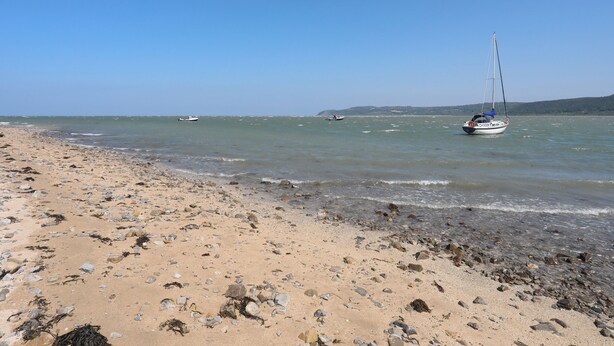 A beach with a sailboat, rocky shore, and calm sea.