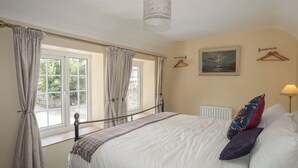A bedroom with a large bed, a window with curtains, a radiator, a hanging light fixture, and a painting on the wall.