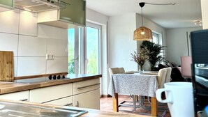 Une cuisine moderne dotée d’une hotte en acier inoxydable, de meubles blancs et d’un plan de travail en bois. On y trouve un coin repas avec une table dressée pour deux personnes, un vase rempli de fleurs et une machine à café.