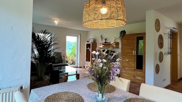 Un coin repas avec une table ronde, des chaises blanches et un luminaire suspendu en fibres tressées.