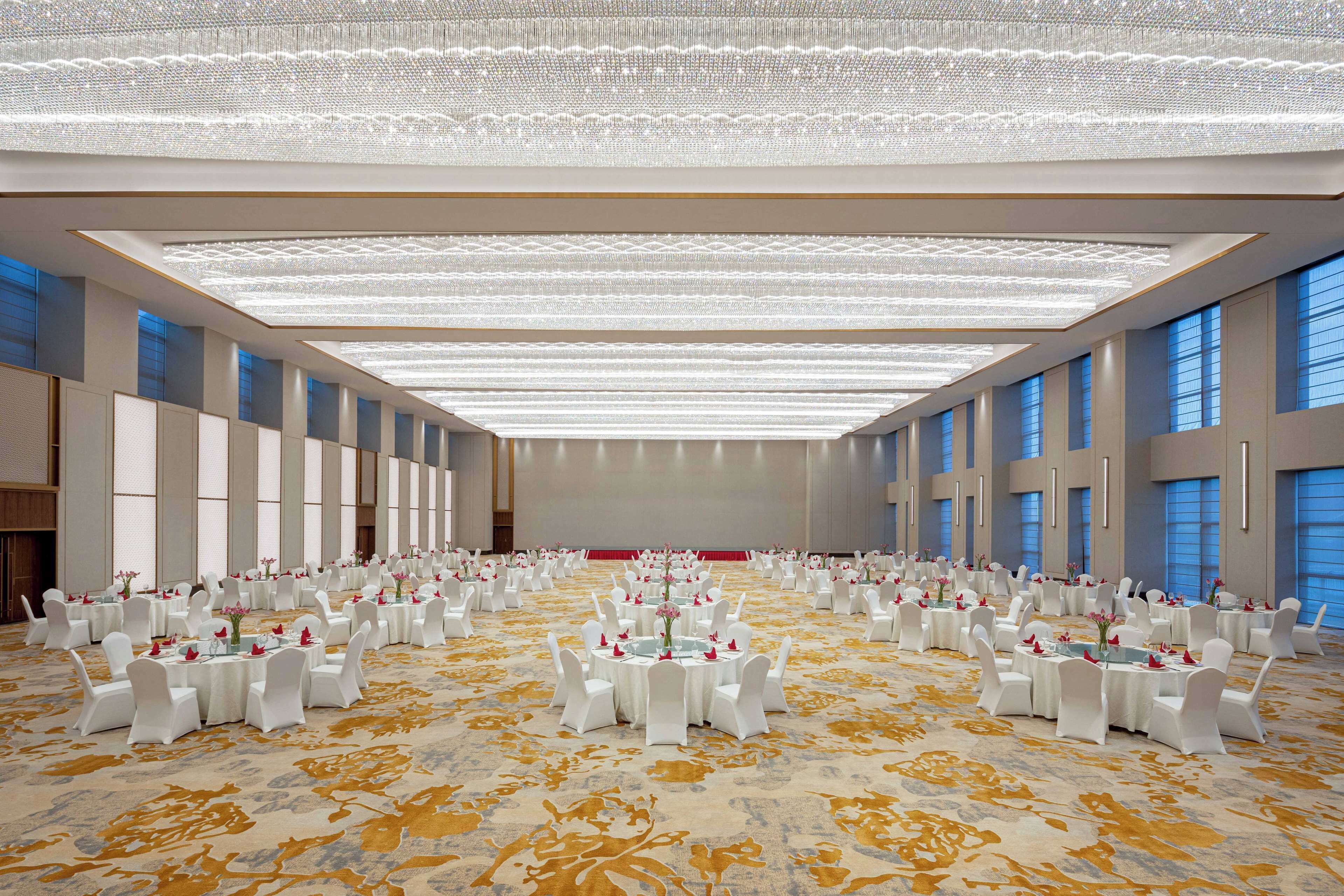 A large, well-lit conference room with rows of round tables, each set with white chairs and floral centerpieces.