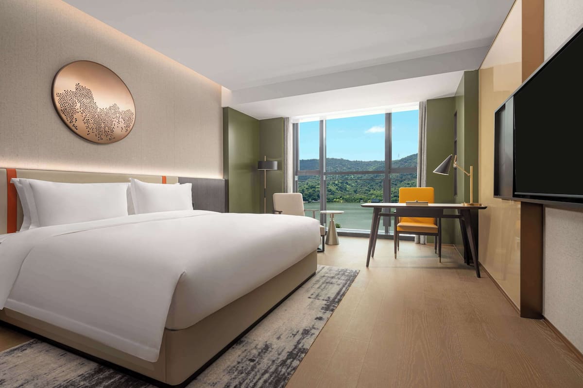 Ein Hotelzimmer mit einem großen Bett, einem Schreibtisch mit Stuhl, einem Flachbildfernseher und Blick auf einen See und Berge.