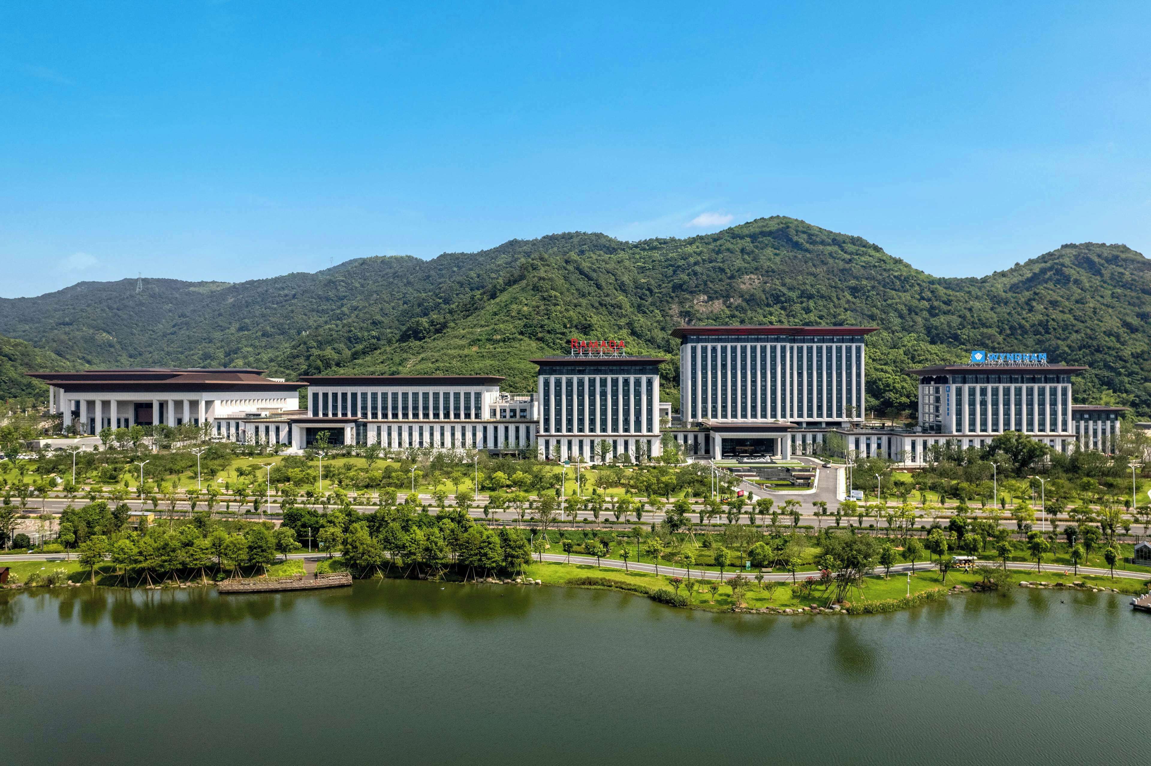 Un ensemble immobilier moderne, avec un grand lac en façade, entouré de verdure et de collines.
