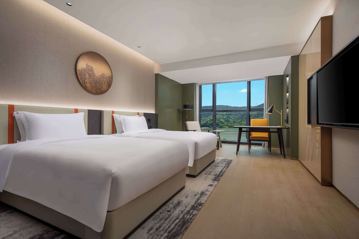 Ein modernes Hotelzimmer mit zwei großen Betten, einem Essbereich mit Tisch und Stühlen, einem Flachbildfernseher und einem großen Fenster mit schöner Aussicht.
