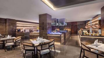 A modern restaurant with a central bar area, multiple dining tables, and a sleek, contemporary design.
