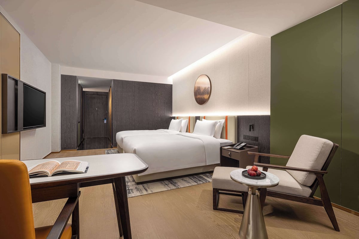 Ein modernes Hotelzimmer mit Bett, Schreibtisch, Stuhl und einem kleinen Tisch mit Obst.