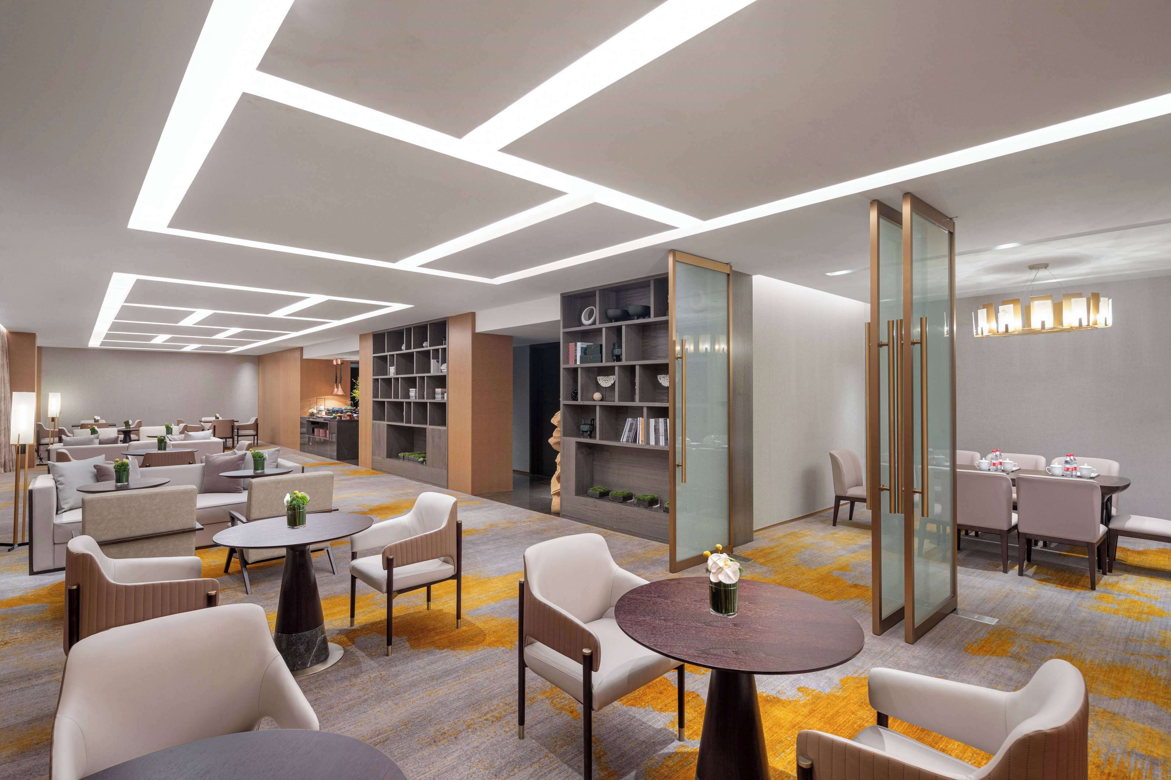 Een moderne hotellobby met zithoeken, een receptiebalie en een boekenkast.