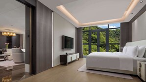 Une chambre moderne avec un grand lit, un téléviseur fixé au mur et une vue sur la verdure grâce à de grandes fenêtres.