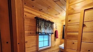 Ein Badezimmer einer Holzhütte mit Toilette, Waschbecken und Fenster mit Vorhängen.