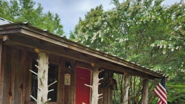 Eine rustikale Holzhütte mit einer Holzterrasse, einer roten Tür und einer US-amerikanischen Flagge.
