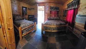 Ein Schlafzimmer in einer Blockhütte mit zwei Betten, einem Deckenventilator und einem Fenster.