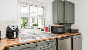 Una cocina con un lavamanos doble, microondas, cafetera y armarios.