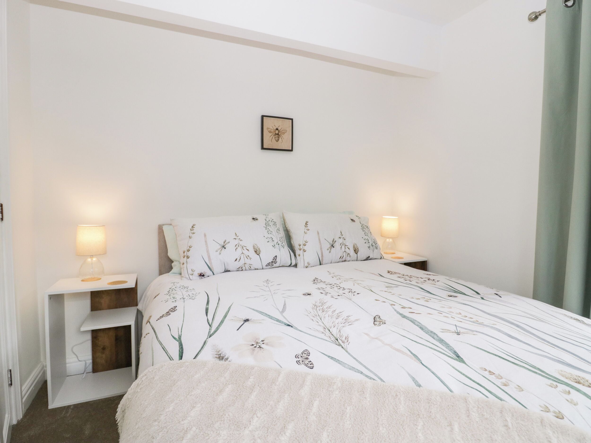 A bedroom with a bed, two bedside tables with lamps, a small shelf, and a framed picture on the wall.