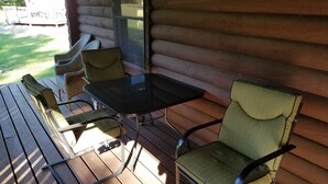 Une terrasse en bois avec une table en verre et quatre chaises.