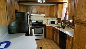 Une cuisine de taille réduite, dotée de meubles en bois, d’un réfrigérateur, d’une cuisinière, d’un four à micro-ondes et d’un évier.