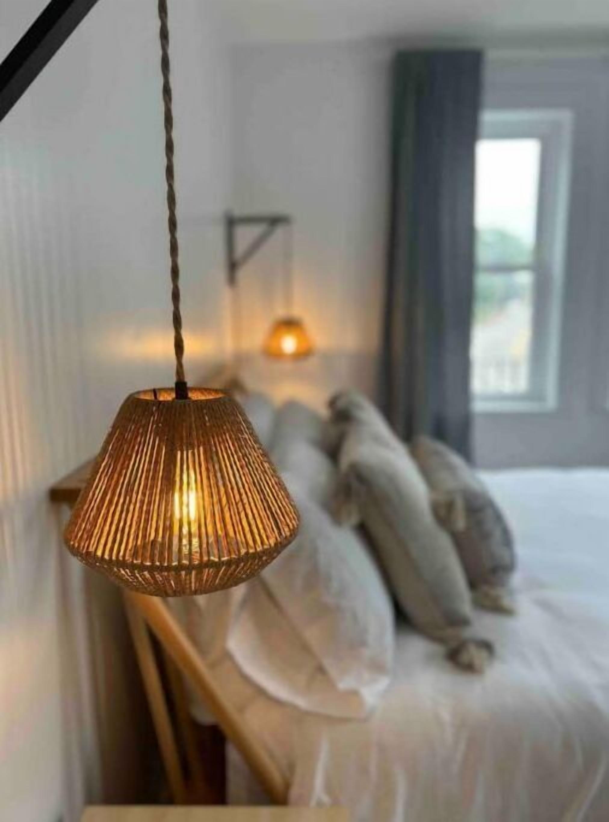 Een slaapkamer met een bed, kussens, een hanglamp en een raam.