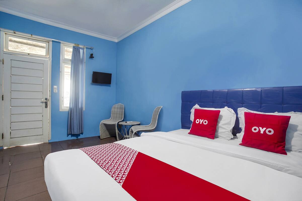 Habitación de hotel con cama, escritorio, dos sillas, televisor y ventana con cortinas.