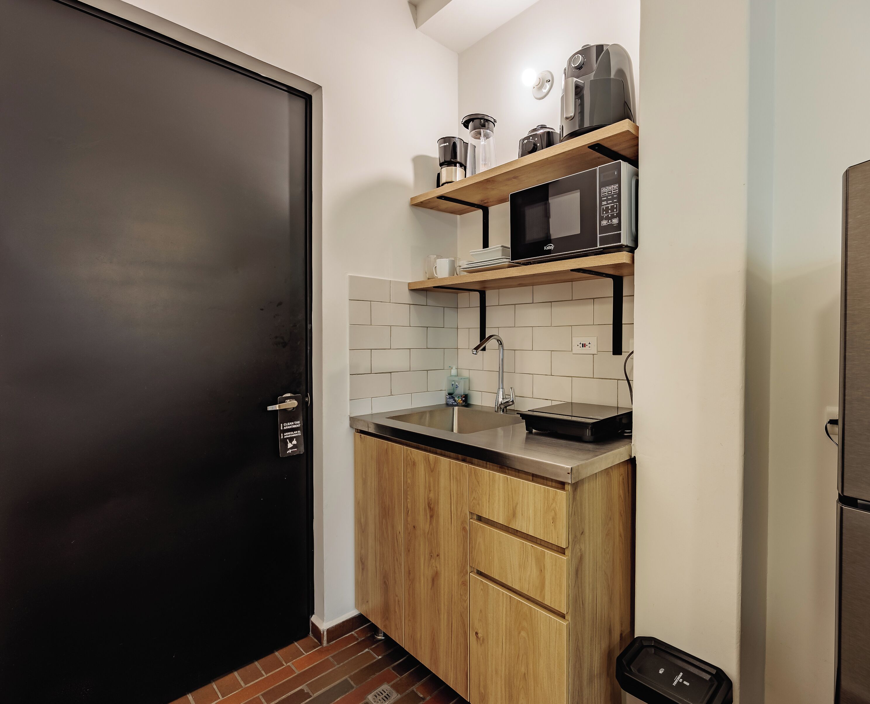 A compact kitchen with a black door, a microwave, a coffee maker, and a sink.