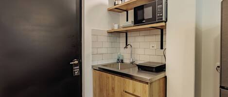 A compact kitchen with a black door, a microwave, a coffee maker, and a sink.