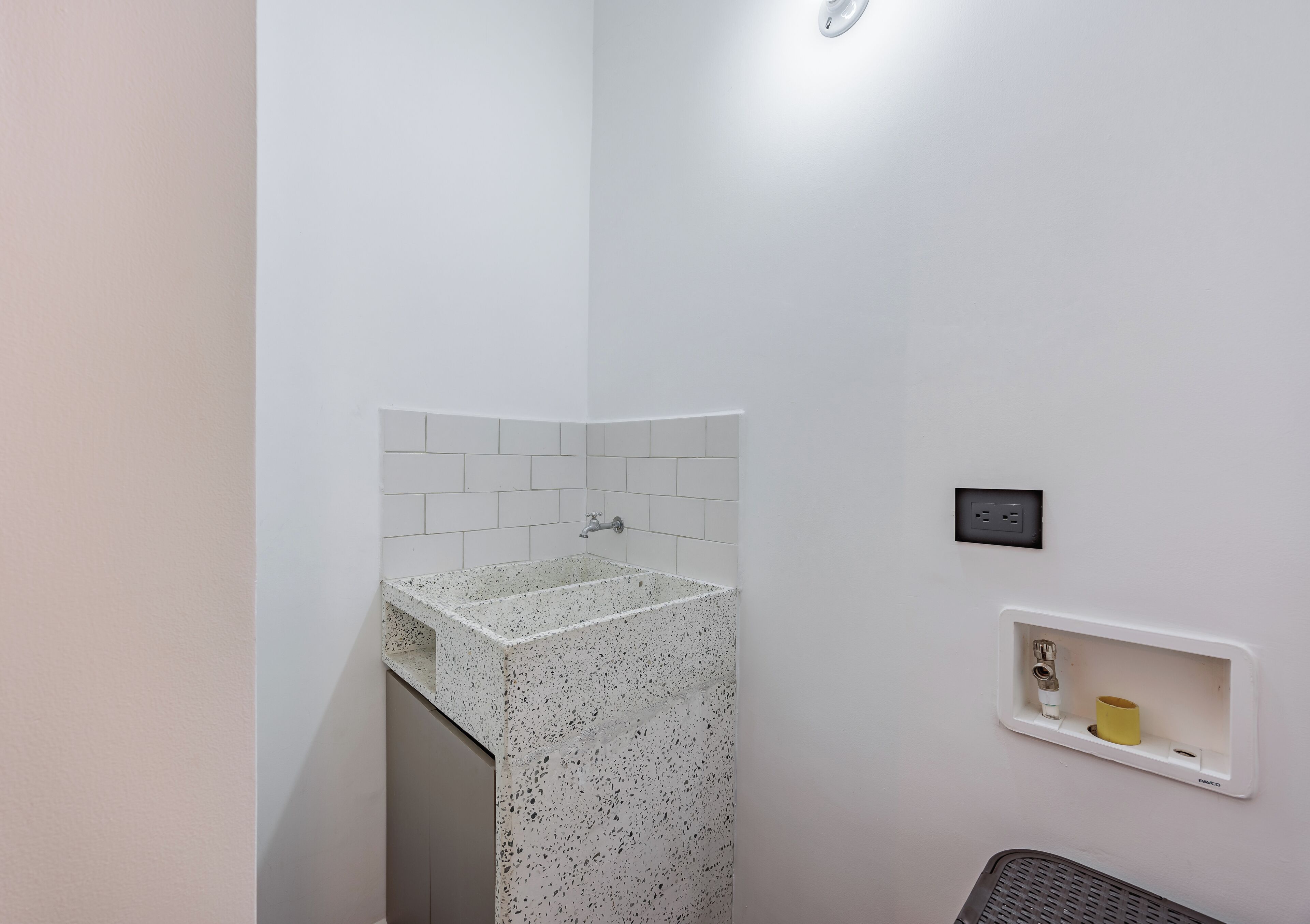 Une salle de bain avec un lavabo à motifs, des murs recouverts de carreaux blancs, une petite étagère avec des articles de toilette et une prise de courant.