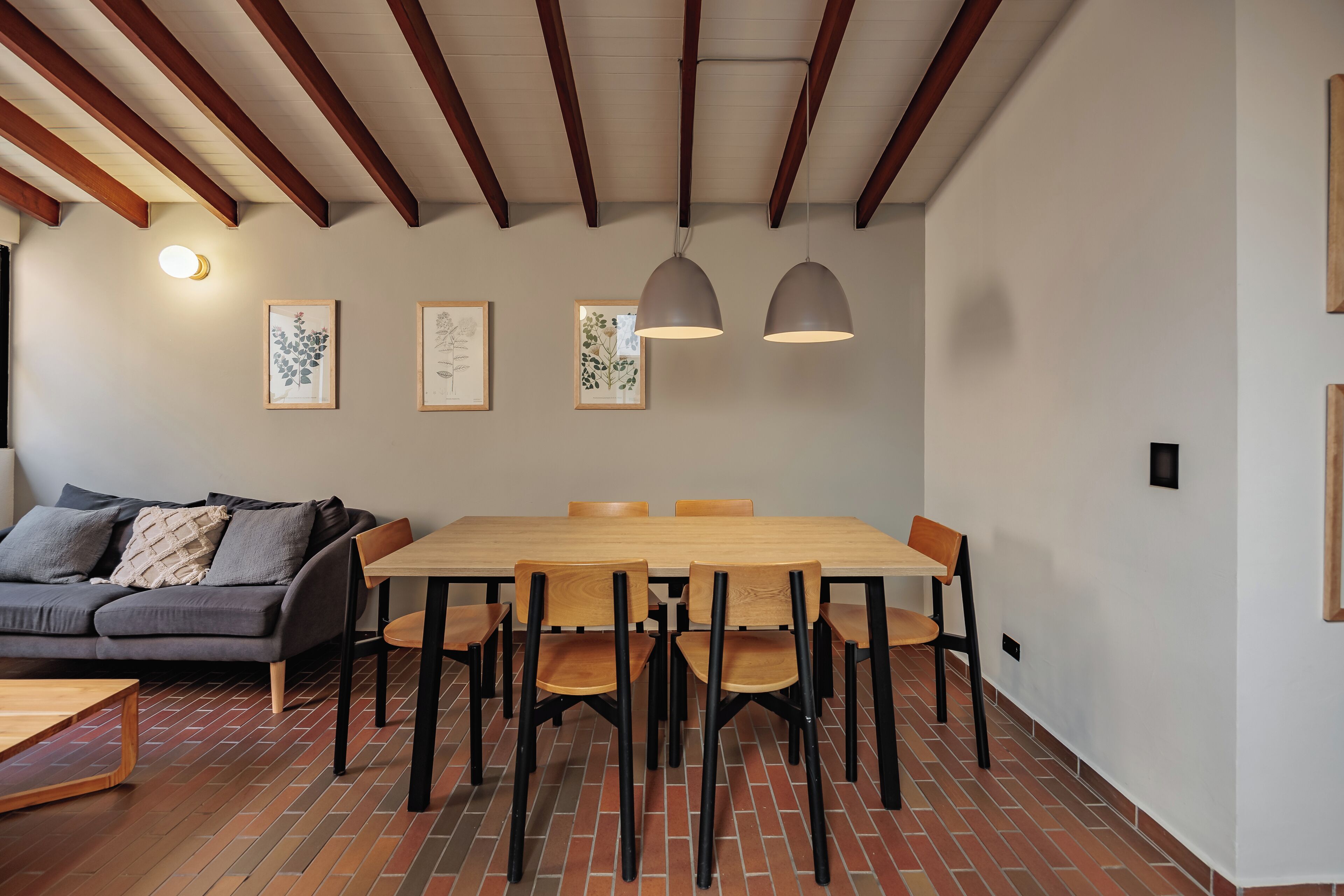 Ein Essbereich mit einem Holztisch, Stühlen, einem grauen Sofa und gerahmten Kunstwerken an der Wand.
