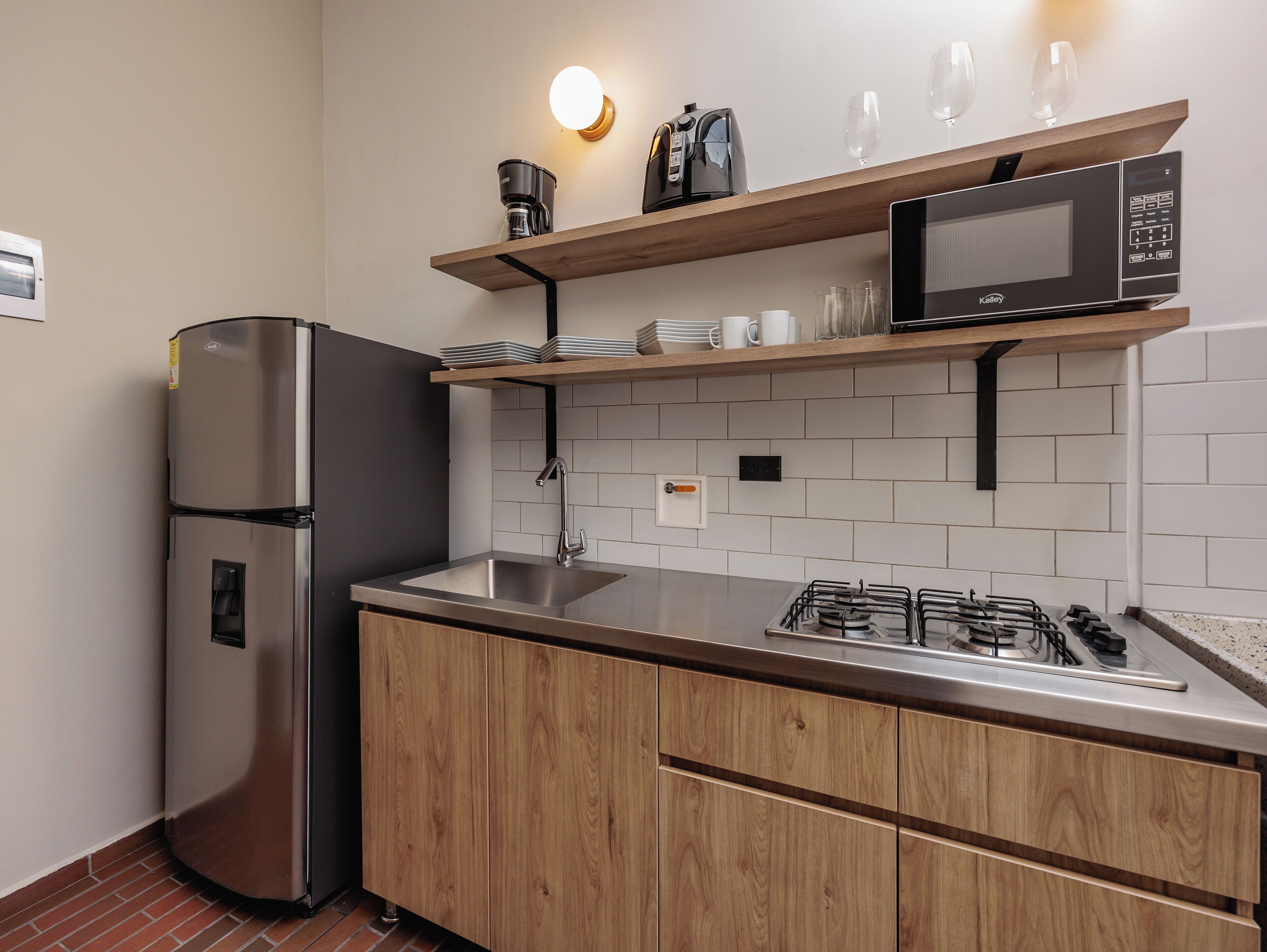 Eine moderne Küche mit einem Edelstahl-Kühlschrank, einem eingebauten Gasherd, Holzschränken, einer Mikrowelle und einem Regal mit Gläsern und Geschirr.