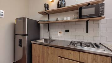 Eine moderne Küche mit einem Edelstahl-Kühlschrank, einem eingebauten Gasherd, Holzschränken, einer Mikrowelle und einem Regal mit Gläsern und Geschirr.