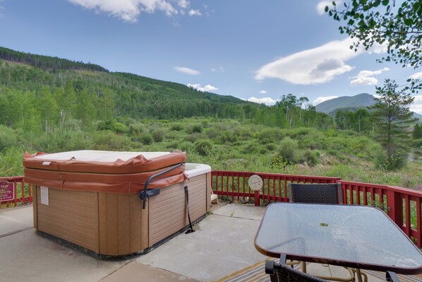 Ein Whirlpool auf einer Terrasse mit Tisch und Stühlen, umgeben von einem roten Geländer, mit Blick auf einen bewaldeten Hang.