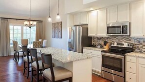 A modern kitchen with white cabinets, stainless steel appliances, and a central island with bar stools. - Two Bedroom at Trillium, NC 3575307 (Cashiers)