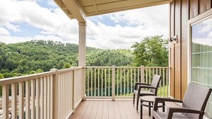 A balcony with a wooden railing, two wicker chairs, and a view of a forested area. - Two Bedroom at Trillium, NC 3575307 (Cashiers)