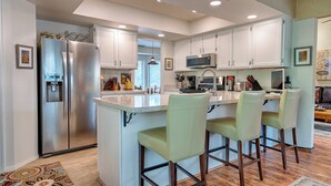A modern kitchen with white cabinets, stainless steel appliances, and a central island with bar stools. - Forest Heights (Flagstaff)