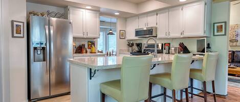A modern kitchen with white cabinets, stainless steel appliances, and a central island with bar stools.