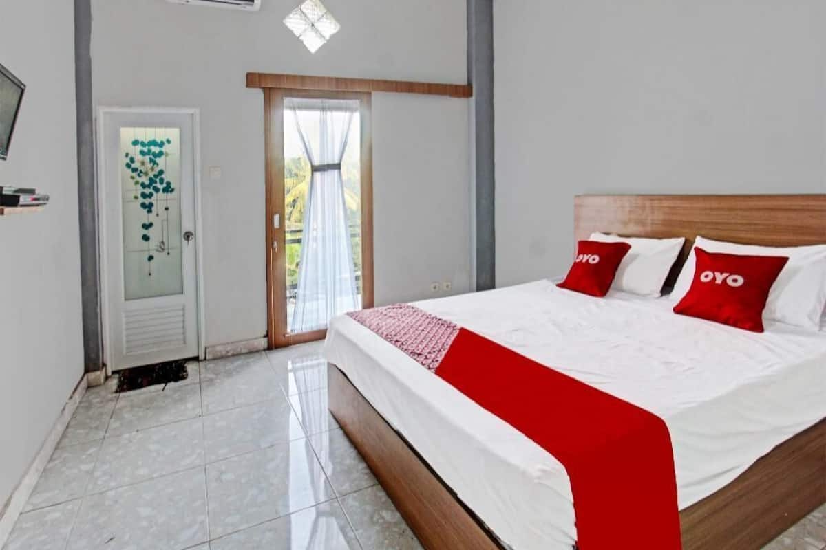Une chambre d’hôtel avec un lit, une porte dotée d’un panneau en verre dépoli et une fenêtre avec des rideaux.