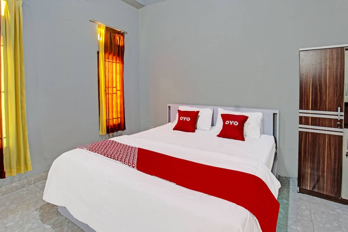 Un lit bien fait, recouvert d’une couette blanche et rouge, avec deux oreillers rouges et un plaid rouge.