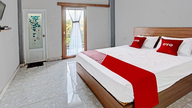 Une chambre d’hôtel avec un lit, une porte dotée d’un panneau en verre dépoli, une fenêtre avec des rideaux et un sol carrelé.