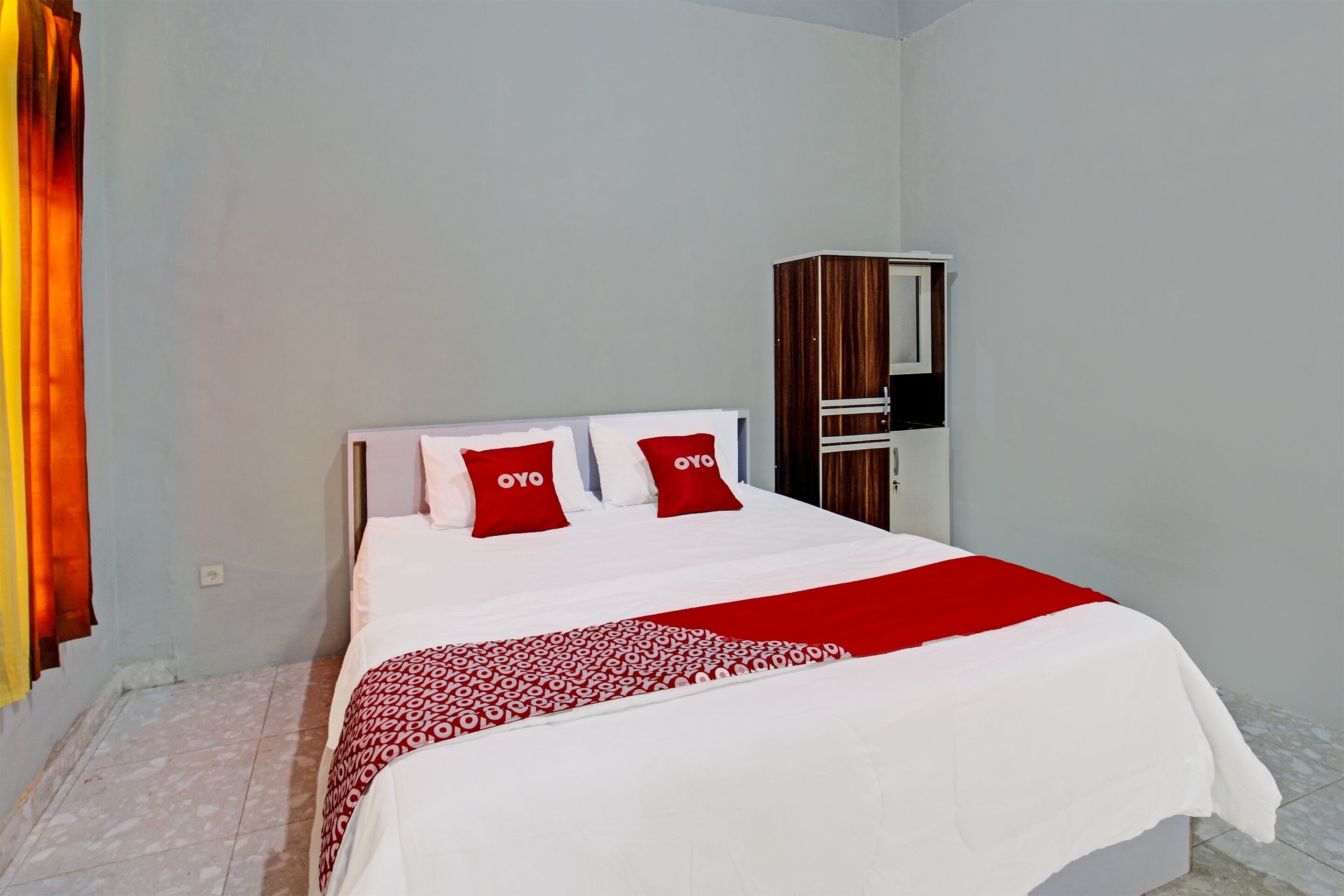 A hotel room with a bed, two red pillows, a white bedspread, and a red and white patterned blanket.