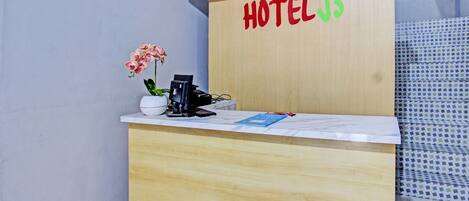 Una recepción de hotel con un mostrador de madera, una orquídea en maceta y un cartel que dice "HOTEL J3".