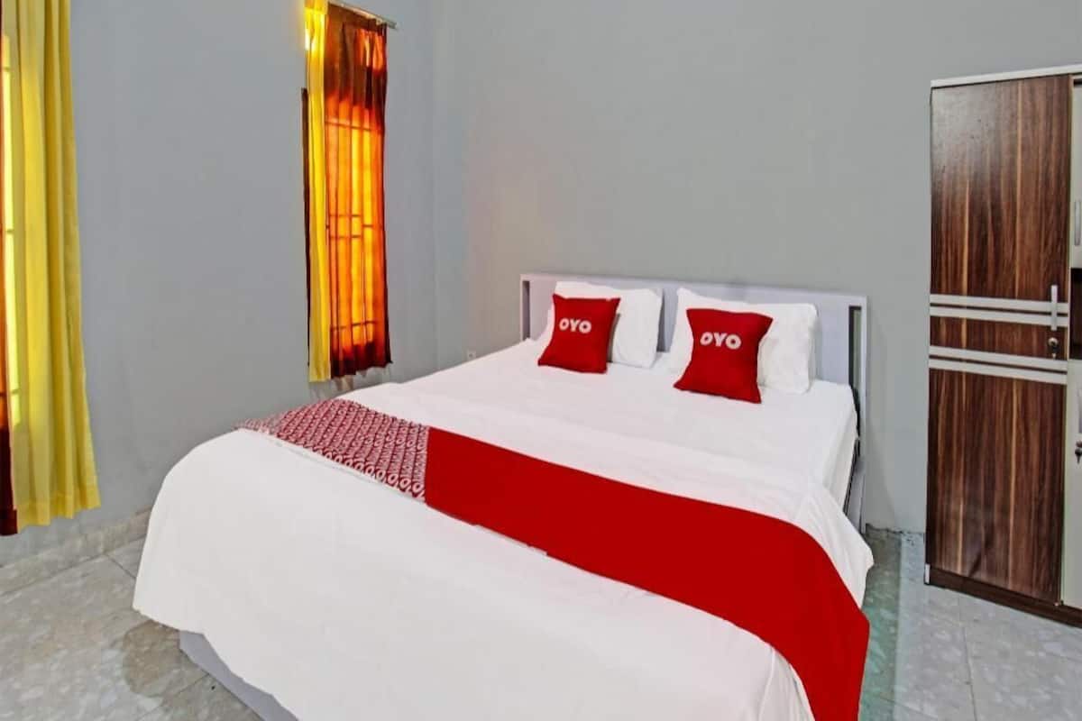 Un lit avec une literie blanche et des touches de rouge, une armoire en bois et une fenêtre avec des rideaux.