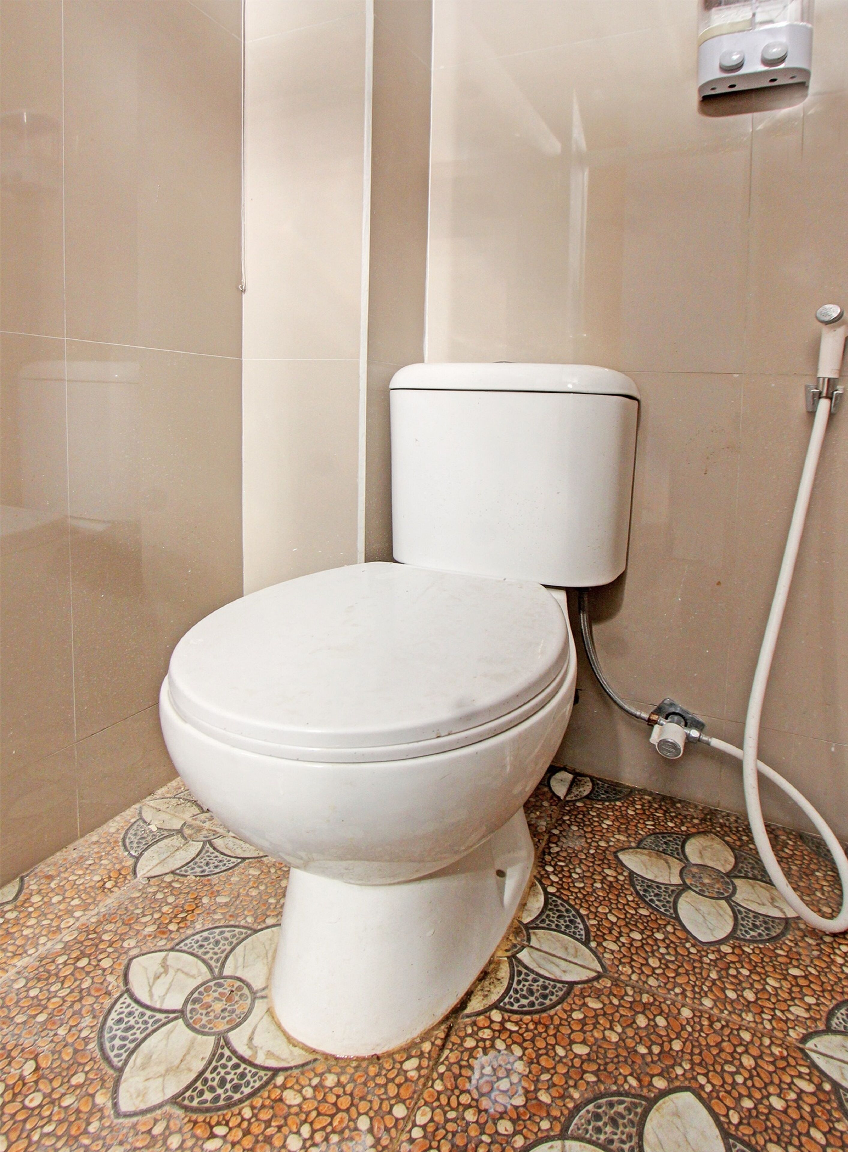 A toilet with a white tank and a floral-patterned floor.