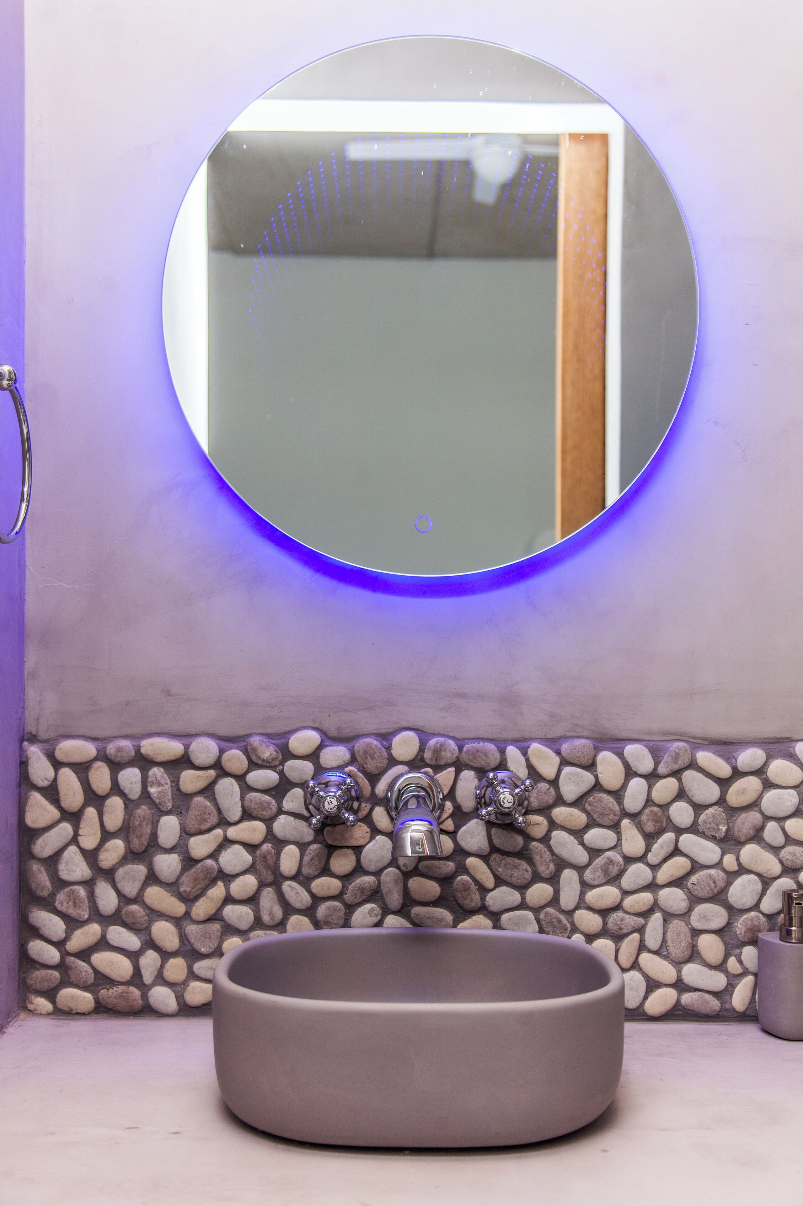 A bathroom with a round mirror, a built-in sink, and a pebble-patterned wall.