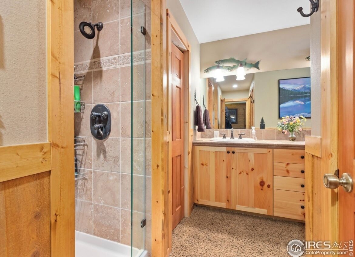 A wooden bathroom with a glass shower enclosure, a sink with a mirror, and a wooden cabinet.