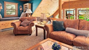 A cozy living room with a wooden ceiling, a sofa, a chair, a coffee table, and a bookshelf.