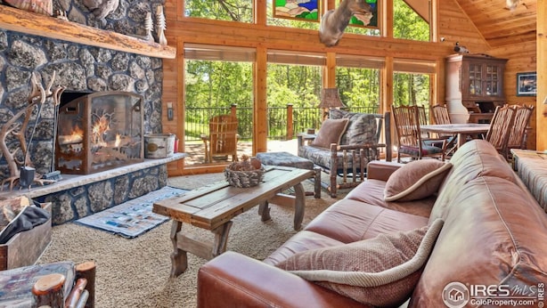 A cozy cabin interior with a stone fireplace, wooden furniture, and large windows offering views of the outdoors.