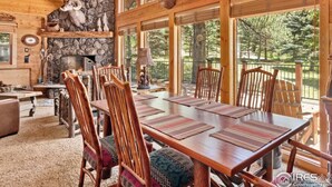 A rustic lodge interior with a stone fireplace, wooden dining table, and chairs.